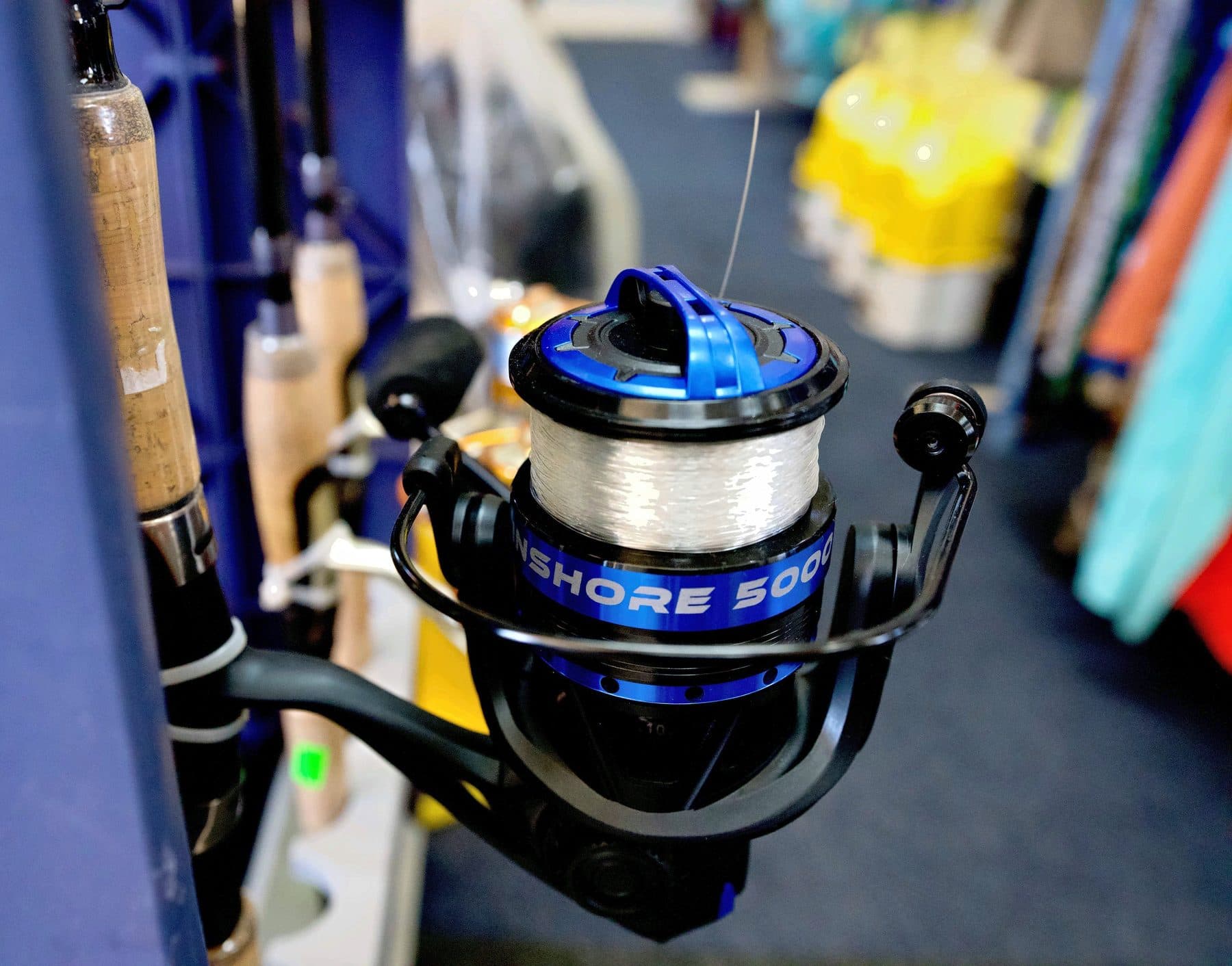 Black and metallic blue spinning reel spooled with clear monofilament on a cork handle rod in a navy rod rack
