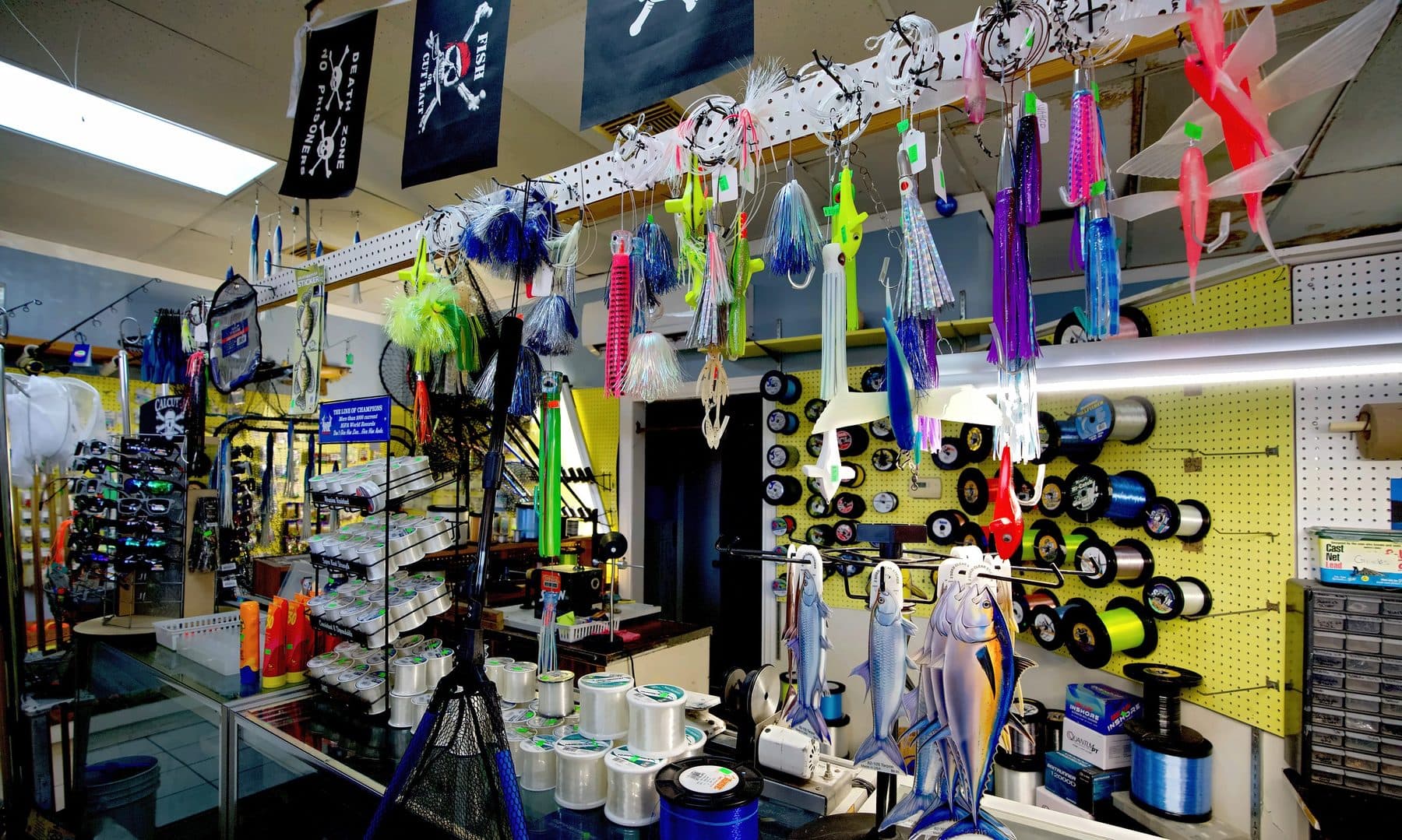 Tackle counter with hanging trolling skirts, flying fish teasers, pirate flags, an Ande line rack and a wall of line spools
