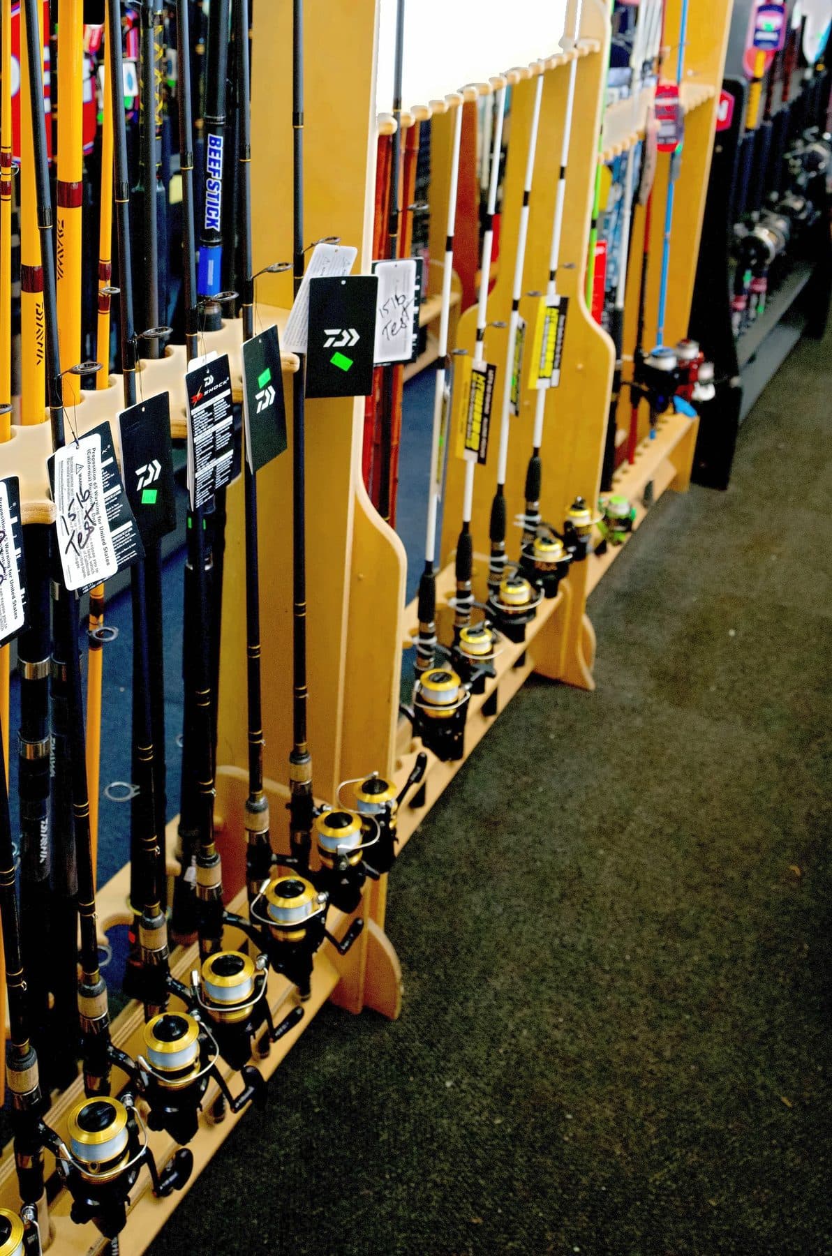Wooden floor racks of Daiwa spinning rod and reel combos with hang tags lining a carpeted tackle shop aisle