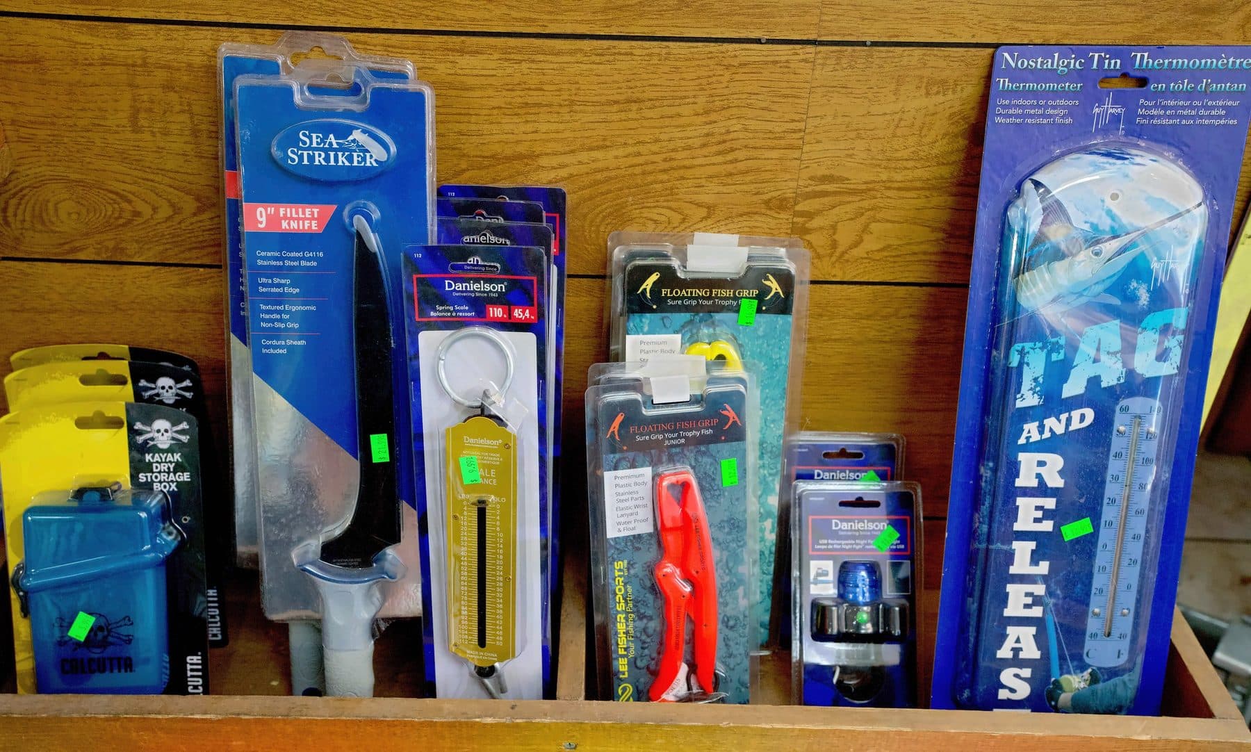 Wooden crate of Sea Striker fillet knives, Danielson spring scales, fish grips, Calcutta dry boxes and a tin thermometer