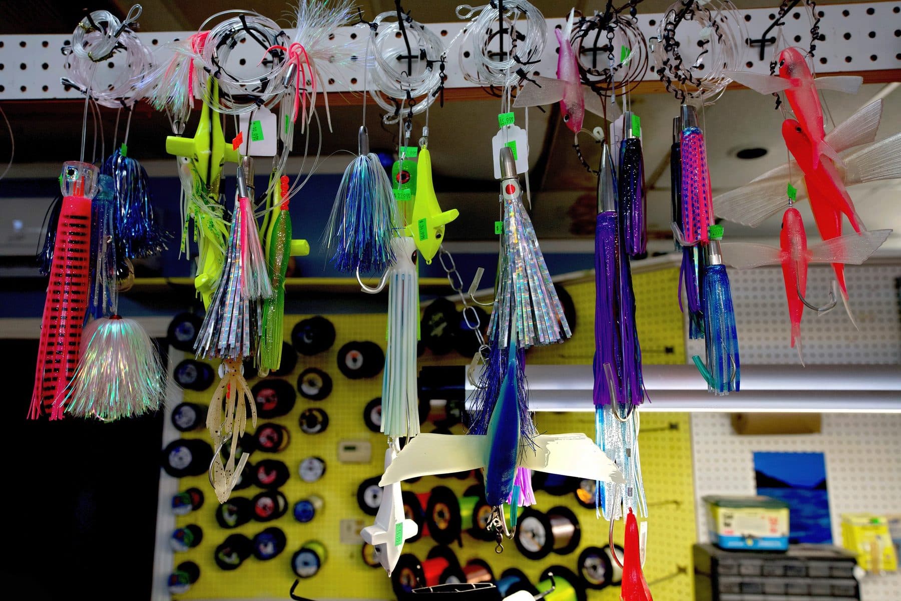 Rigged trolling lures, bird teasers and flying fish baits hanging from pegboard in front of a yellow wall of line spools