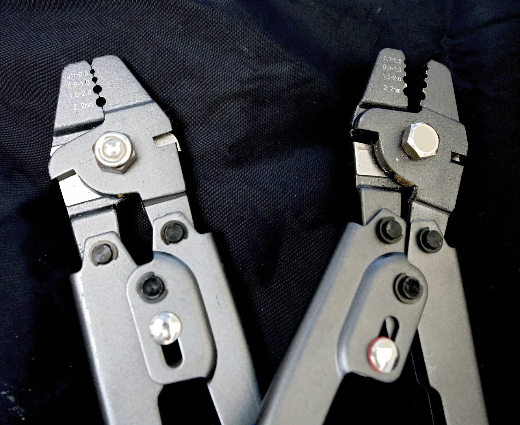 Close-up of two leader crimping tool jaws stamped with die sizes 0.1 to 2.2mm against a dark background
