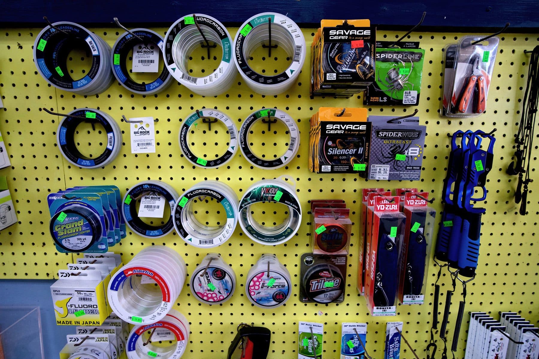 Yellow pegboard wall of fluorocarbon leader spools, Savage Gear and Spiderwire braid, Yo-Zuri Bonita lures and lip grips