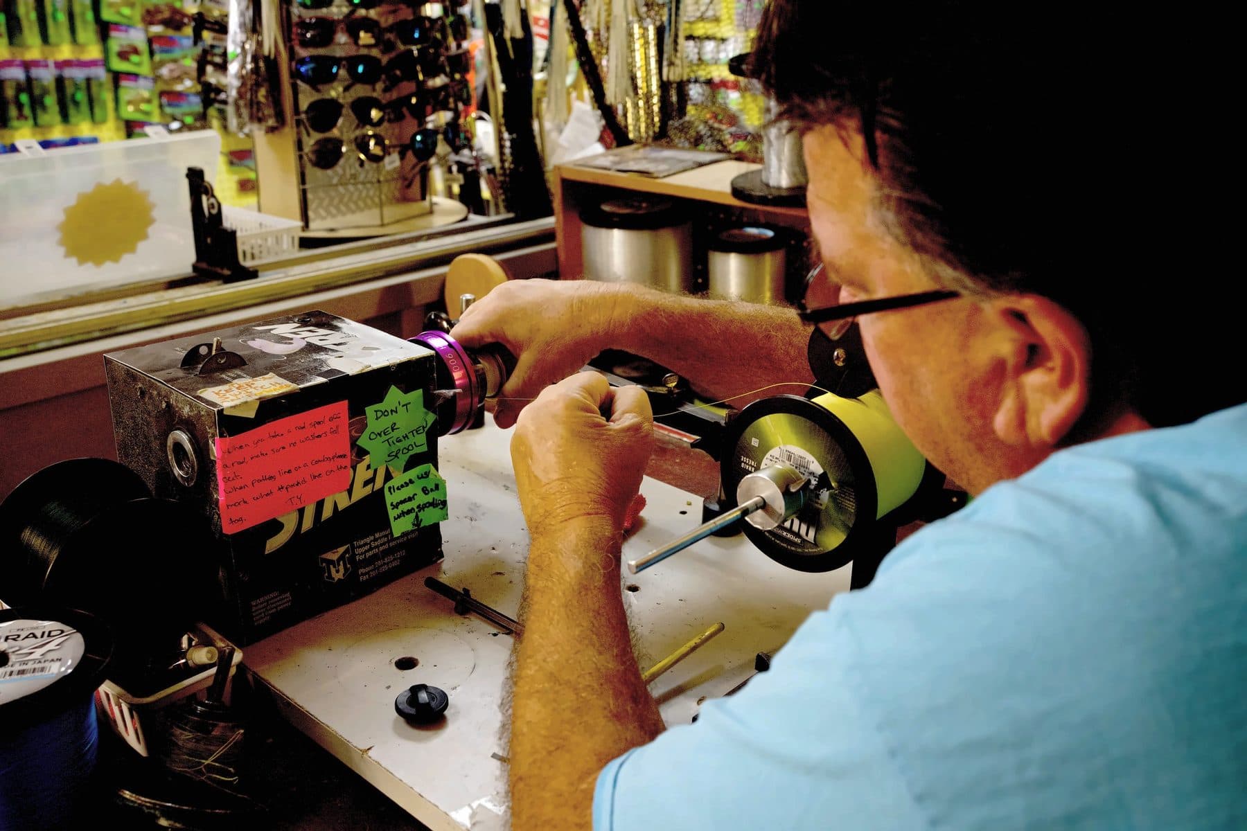 Over the shoulder view of a crew member guiding yellow SpiderWire braid onto a reel spool at the winding machine