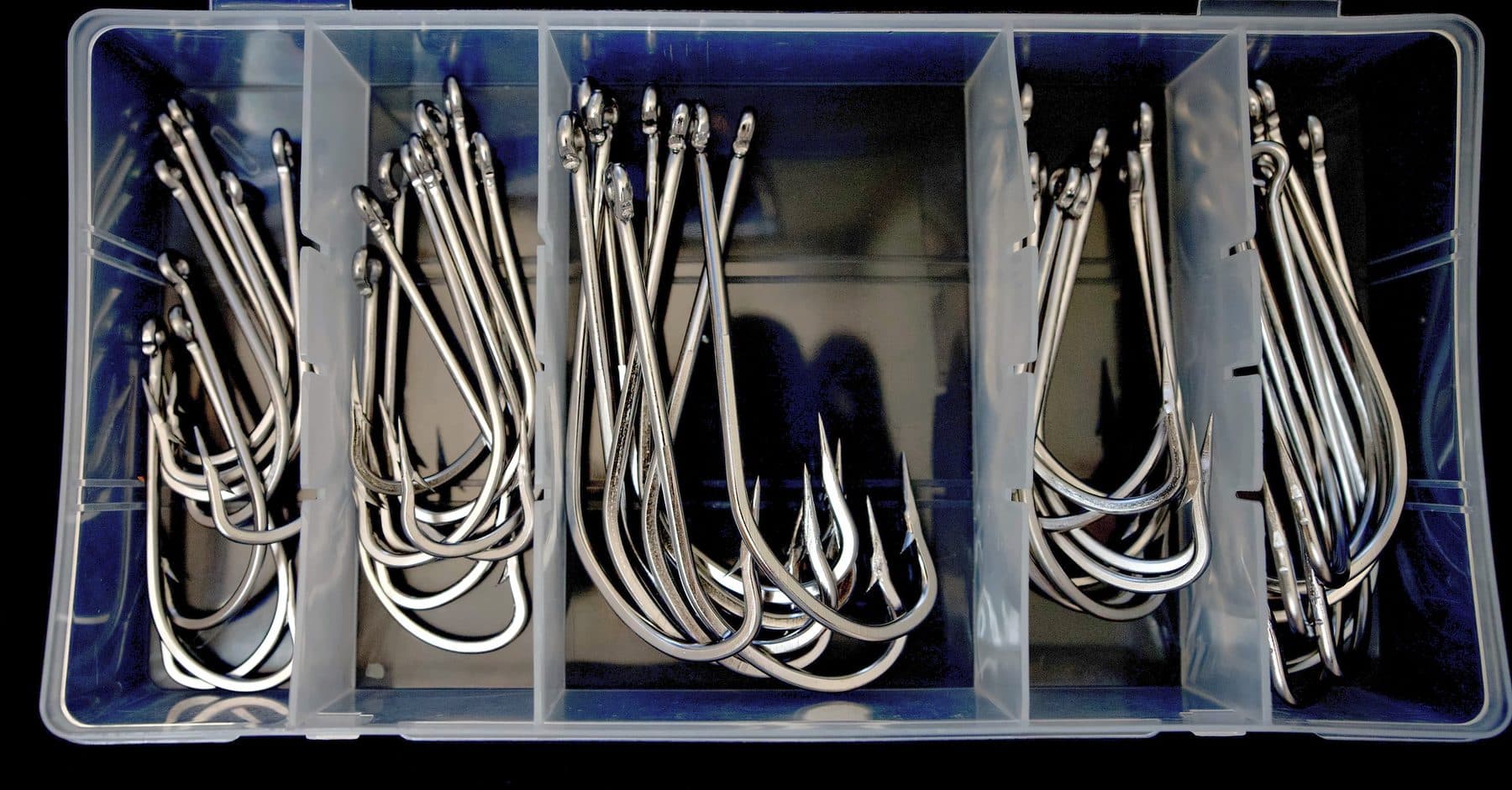 Open clear tackle box of heavy stainless long shank ballyhoo hooks sorted into five compartments