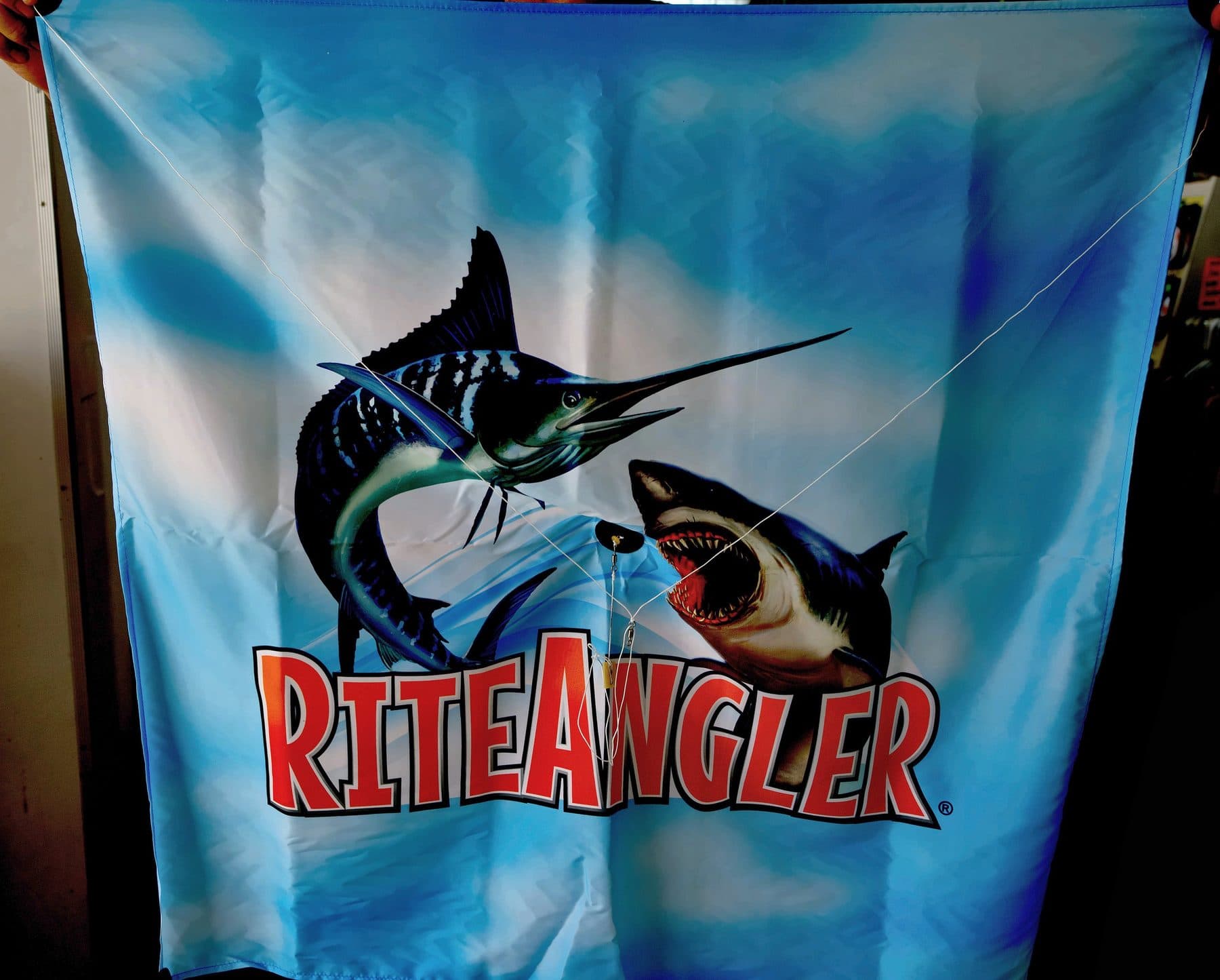 Rite Angler fishing kite with marlin and shark artwork, held open to show its crossed bridle lines and release clip