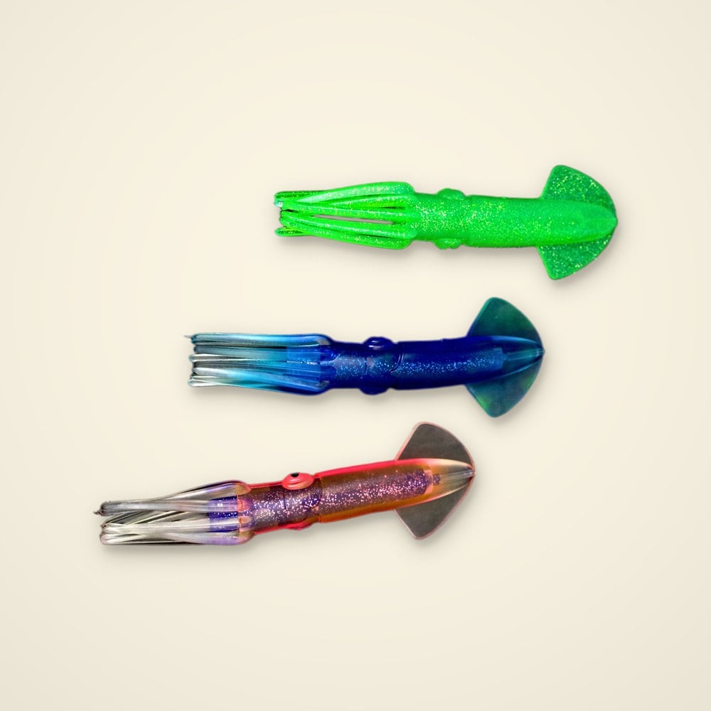 Three soft plastic trolling squid lures in green glitter, blue glitter and pink with purple glitter